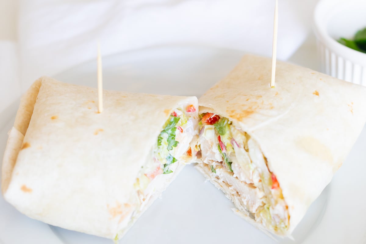 A chicken wrap recipe on a white plate, cut in half.