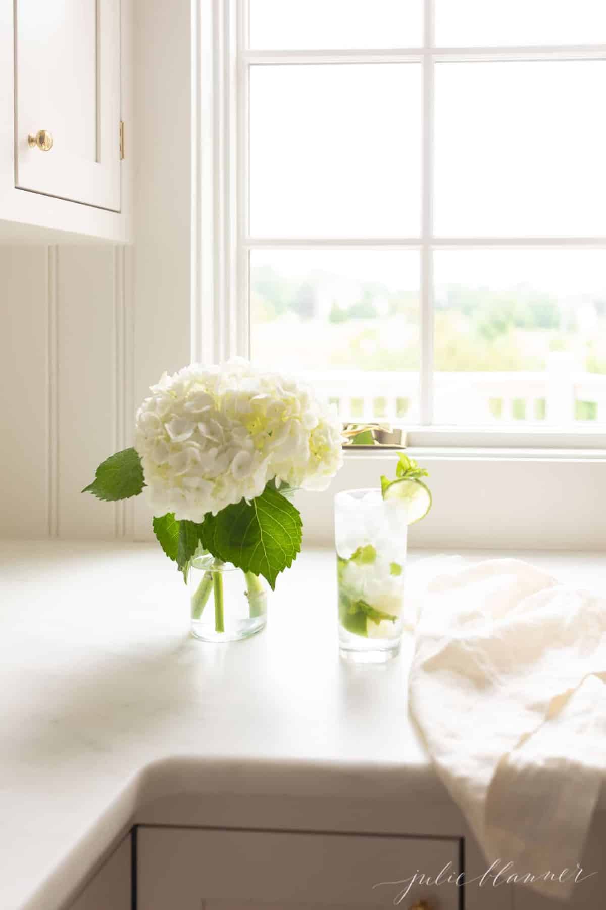 white countertop featuring a vase of hydrangea and a tall clear glass with a mojito.