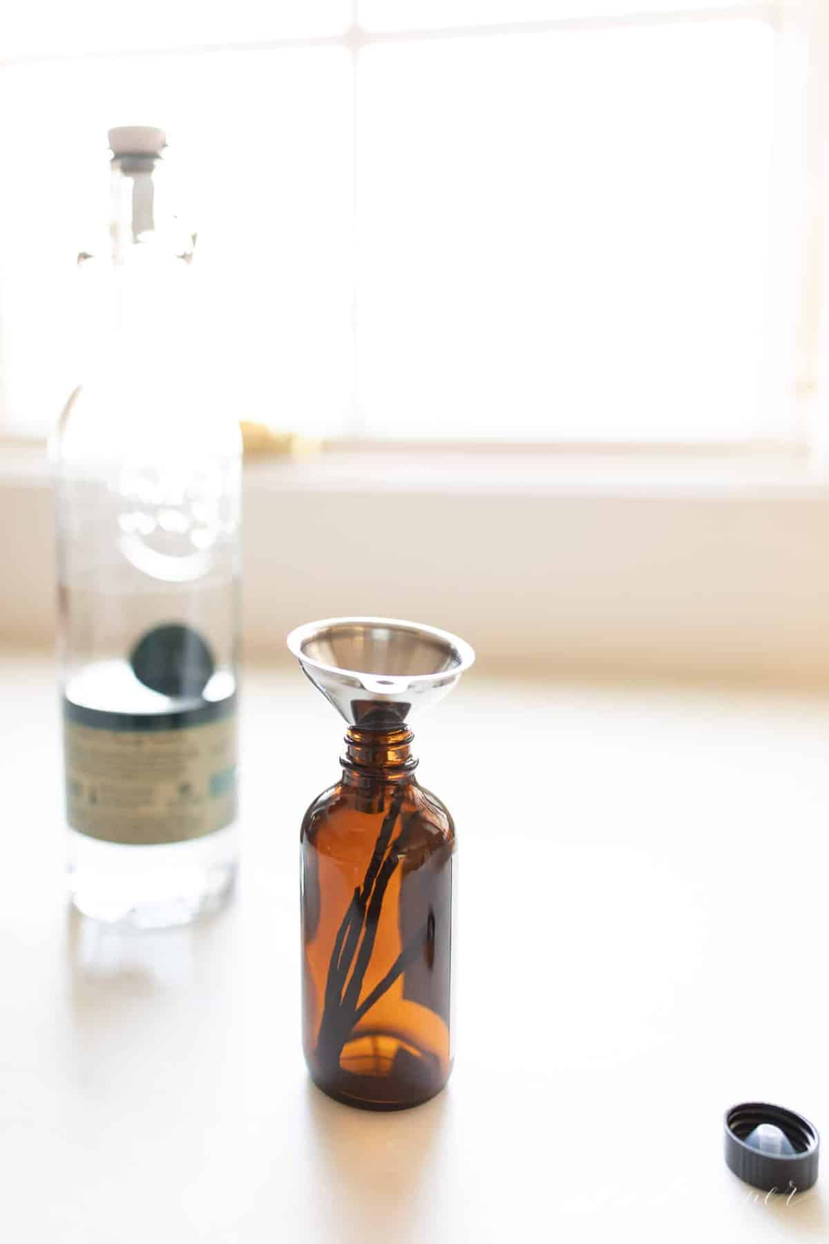 Homemade vanilla extract in an amber bottle and vodka on a white countertop. #homemadevanillaextract #vanilla #vanillabean