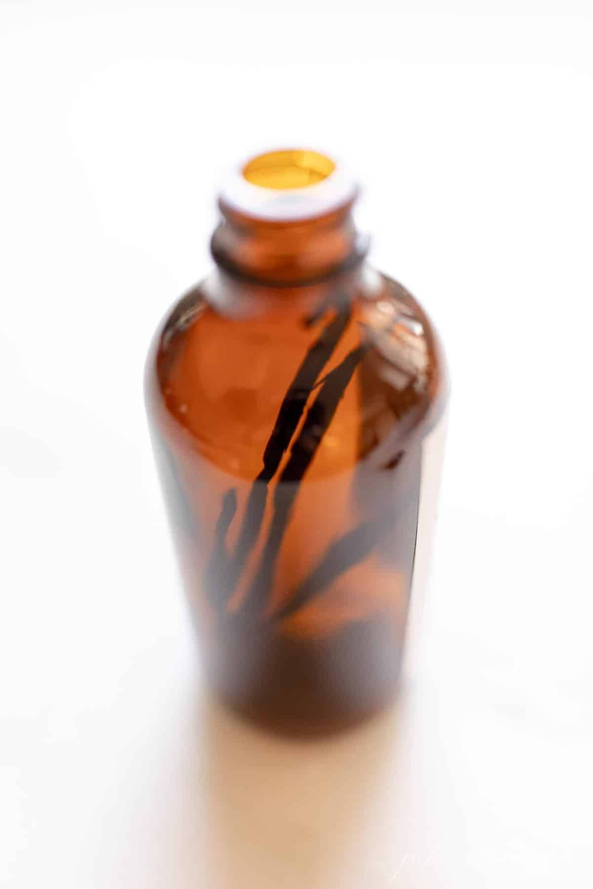 Amber bottle filled with vanilla beans on a white countertop.