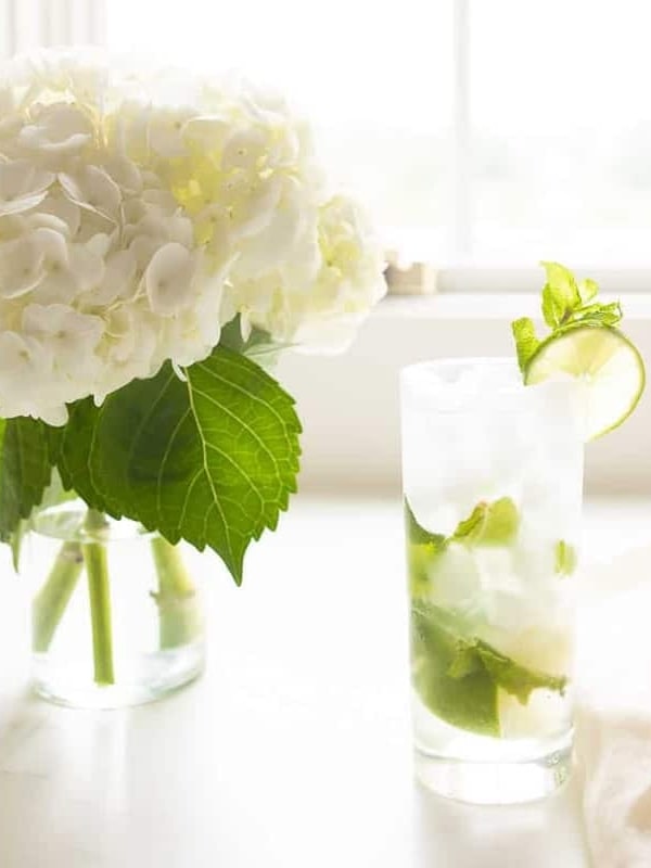 white countertop featuring a vase of hydrangea and a tall clear glass with a mojito.