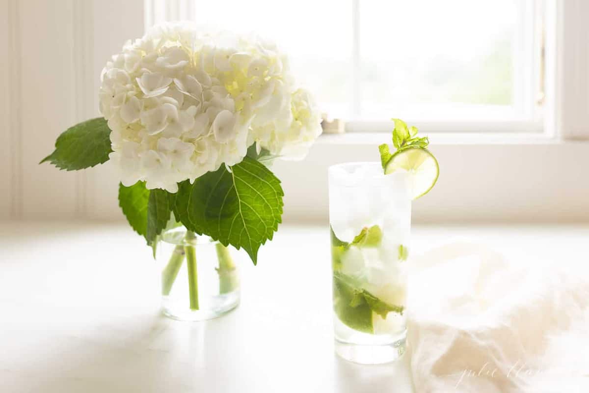white countertop featuring a vase of hydrangea and a tall clear glass with a mojito.