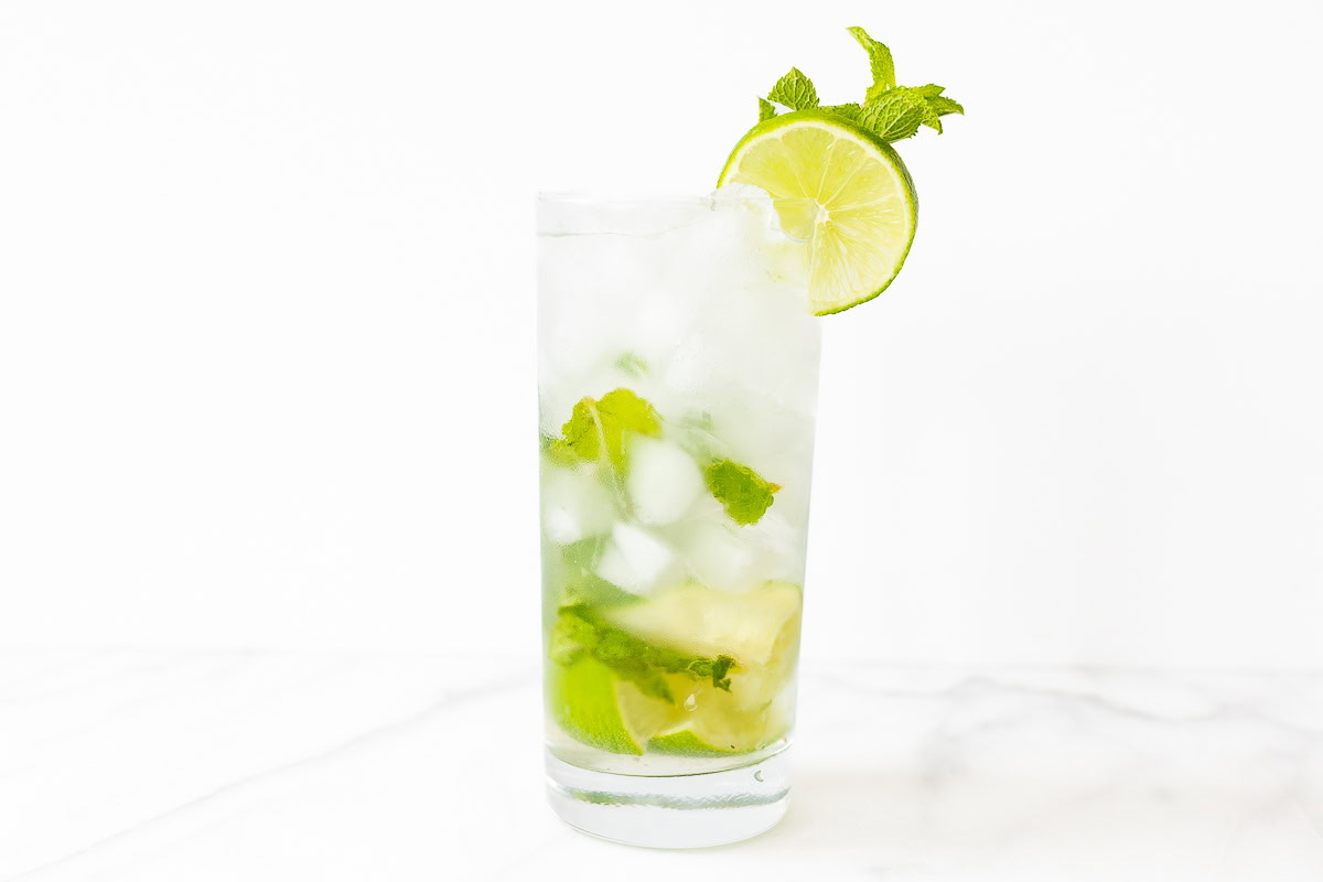 A refreshing mojito cocktail recipe with lime slices and mint leaves, served in a tall glass with ice, against a white backdrop.