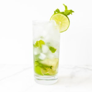 A glass of mojito with lime slices and mint leaves on a marble surface showcases the perfect mojito recipe.