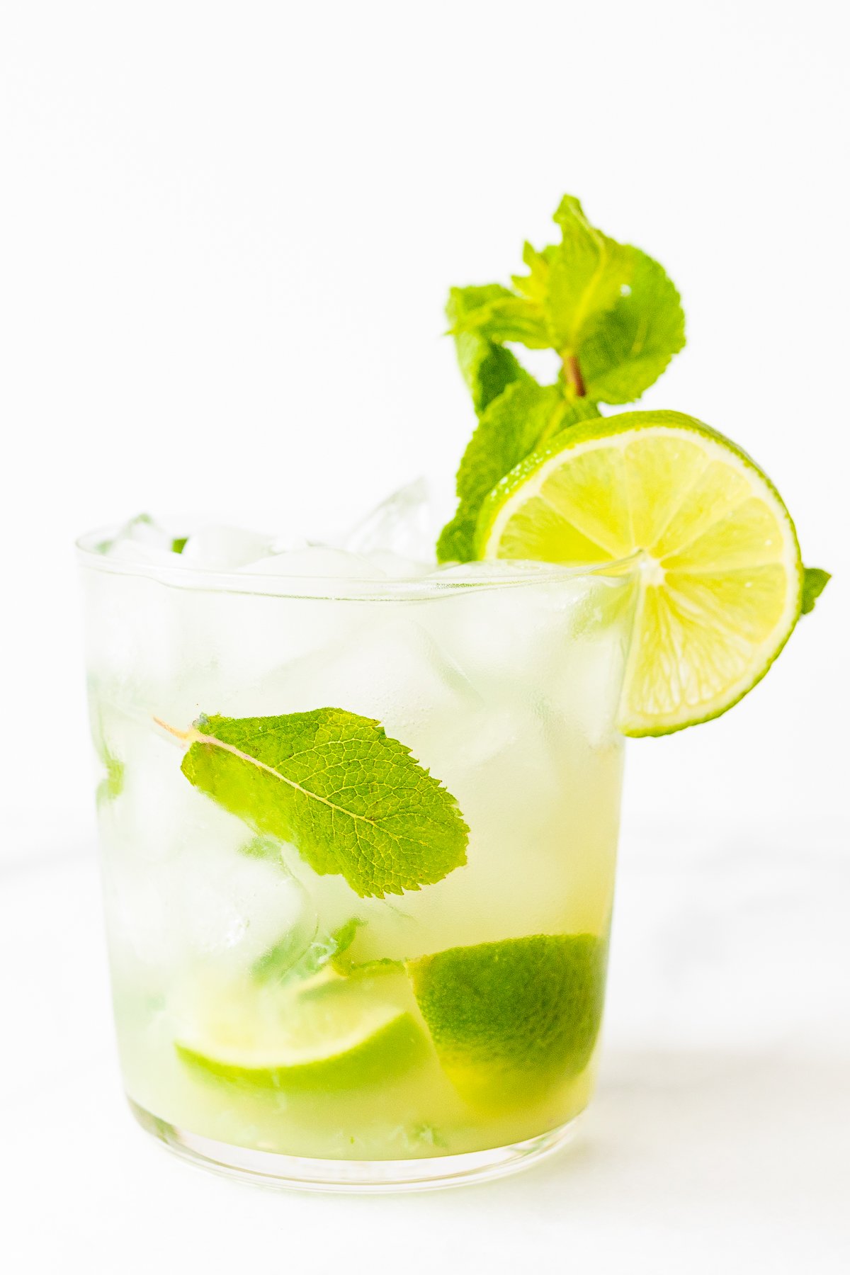 A glass of skinny mojito with lime slices, mint leaves, and ice cubes on a white background.