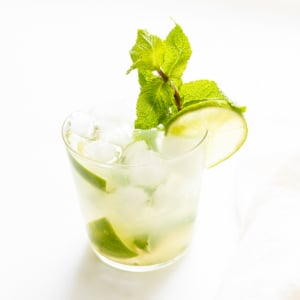 A glass of skinny mojito cocktail with lime slices, ice cubes, and fresh mint leaves, on a white background.