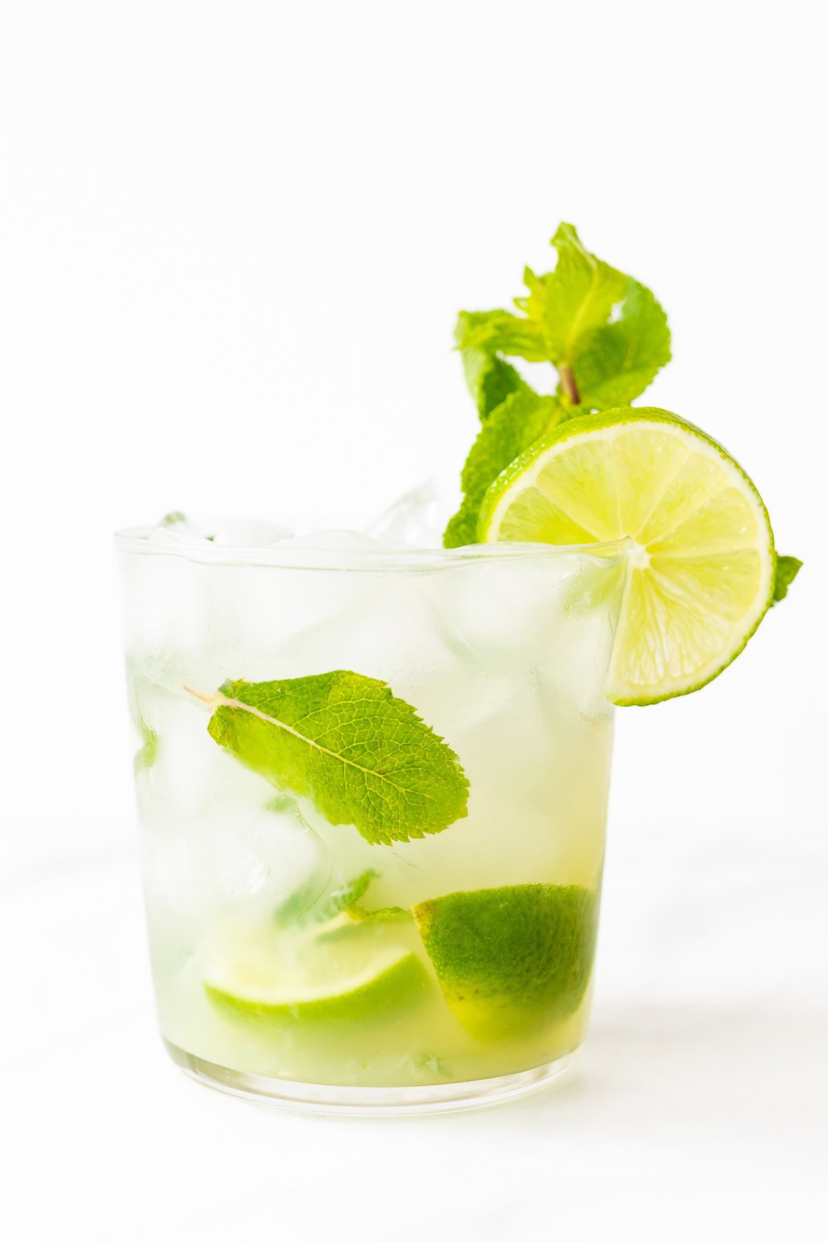 A refreshing skinny mojito cocktail with lime slices and mint leaves in a clear glass against a white background.
