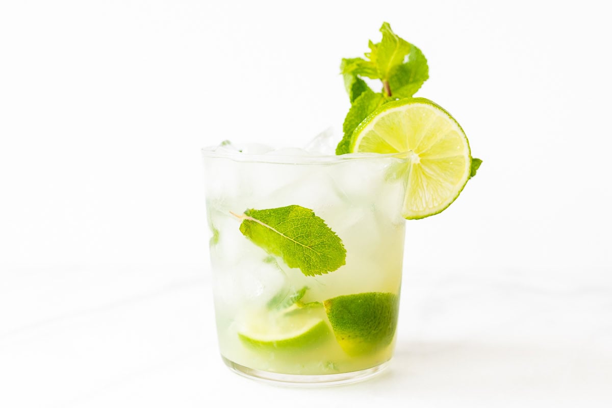 A glass of skinny mojito with lime slices and mint leaves, served with ice on a white background.