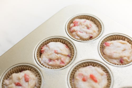 Strawberry muffins batter in a gold muffin tray, sprinkled with sugar, ready for baking.