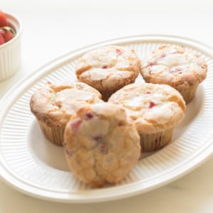 A plate of freshly baked strawberry muffins on a white textured plate, soft lighting, neutral backdrop.