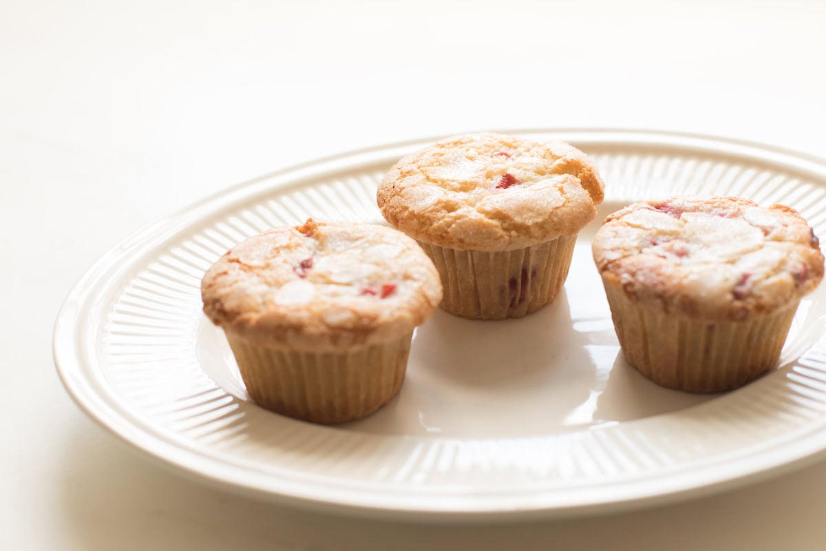 Three strawberry muffins on a white ceramic plate against a light backdrop.