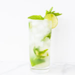 A tall glass of vodka mojito with ice, fresh mint, and a slice of lime on a white background.