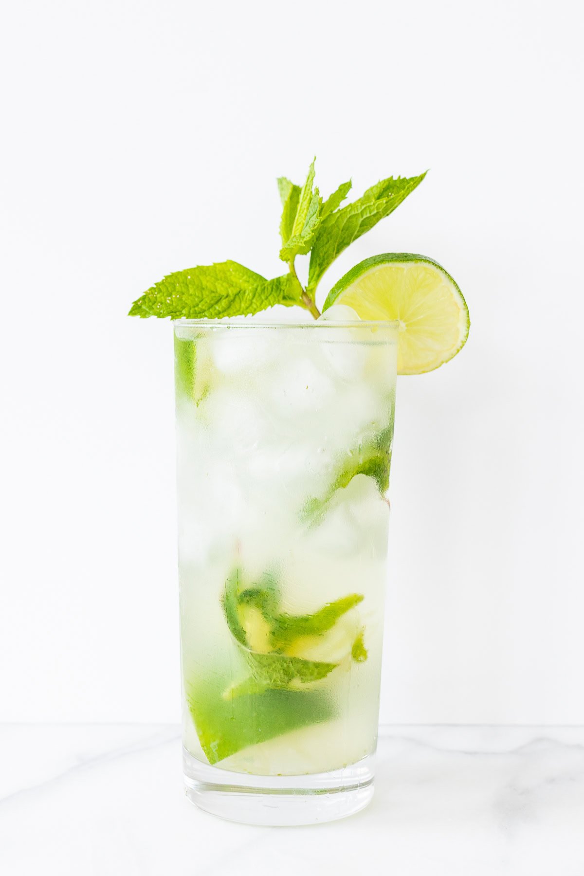 A refreshing vodka mojito cocktail in a tall glass garnished with lime and mint on a white background.