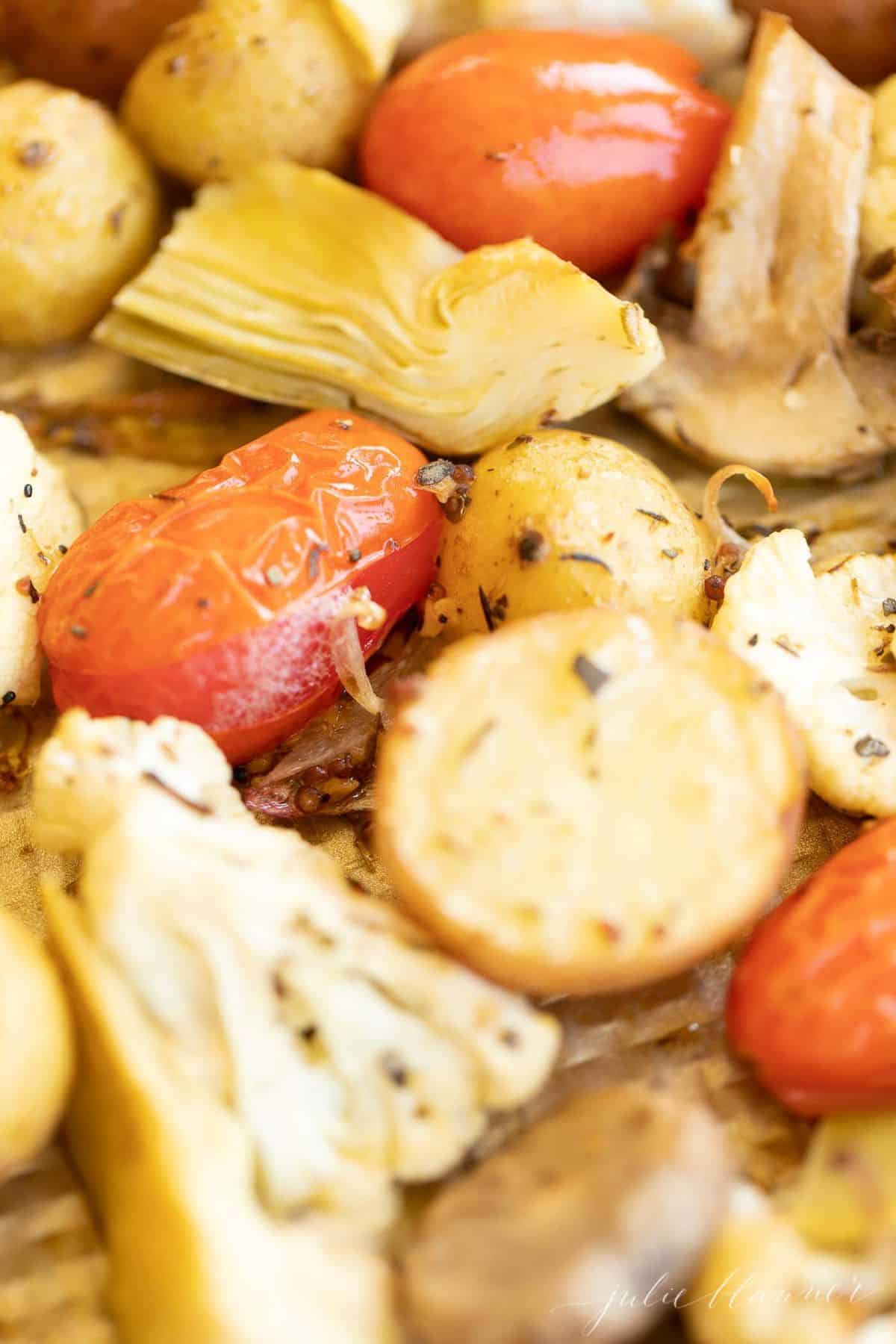 Close-up of roasted grape tomatoes, baby potatoes and artichokes, roasted on a sheet pan.