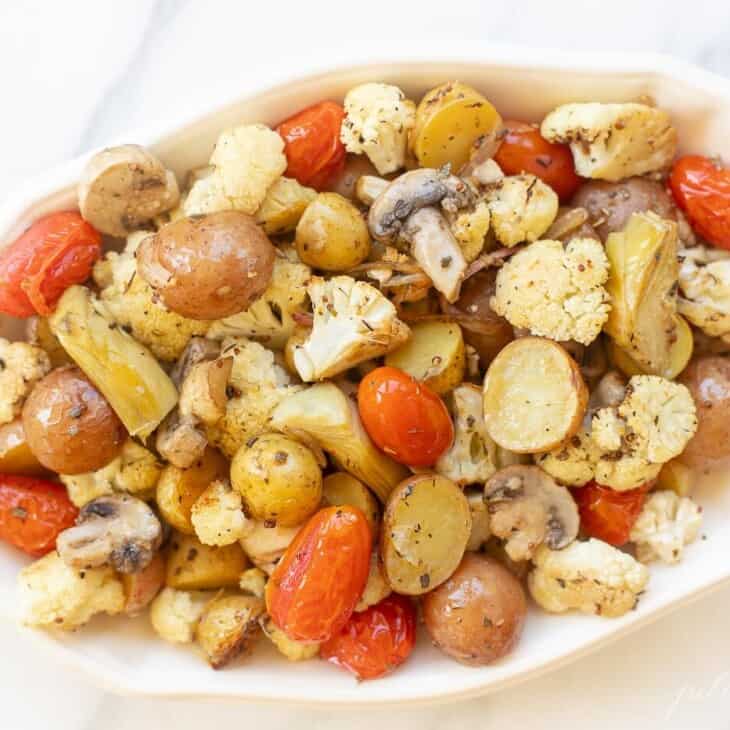 Ivory oval ceramic bowl filled with roasted Italian vegetables, on a white counter . #italianvegetables #roasteditalianvegetables