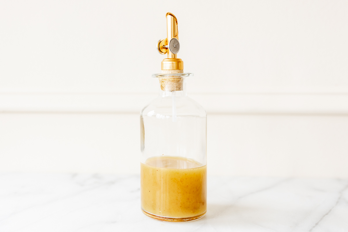 A bottle of apple cider vinaigrette with a gold handle sitting on top of a marble counter.