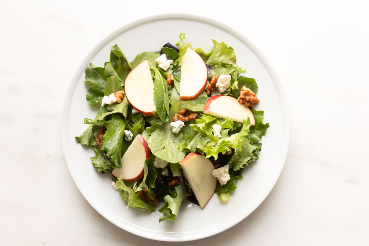 A salad with apples and walnuts, drizzled with apple cider vinaigrette on a white plate.