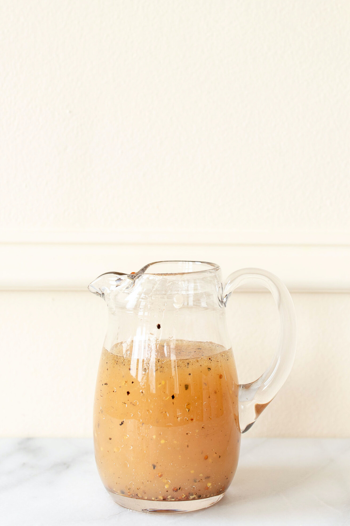 A glass jug with apple cider vinaigrette dressing in it.