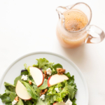 A plate with a salad dressed in apple cider vinegar dressing and a pitcher of juice.