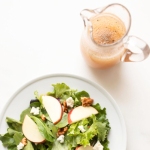 A plate with a salad dressed in apple cider vinegar dressing and a pitcher of juice.