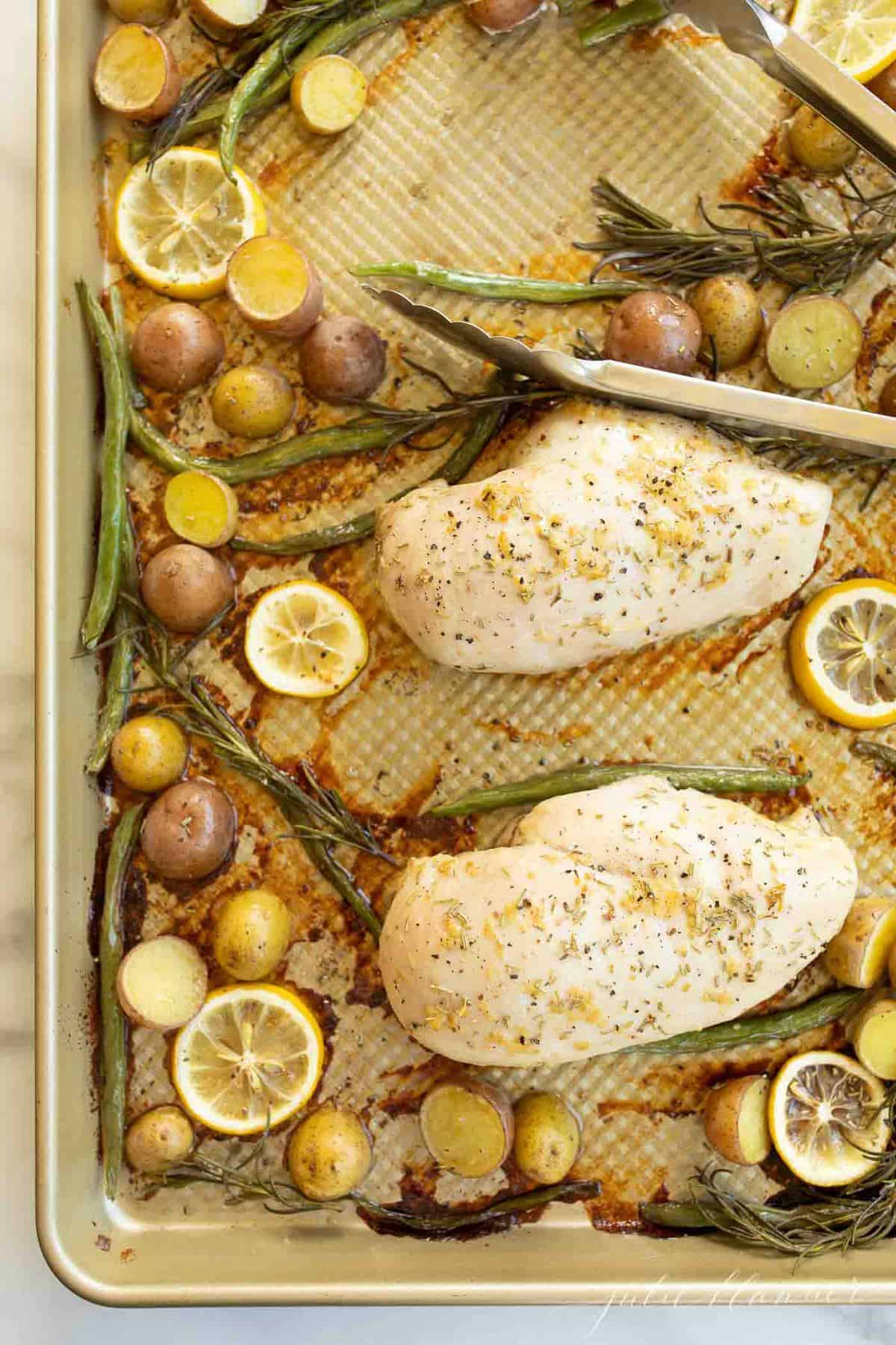 Gold sheetpan filled with baked chicken and veggies such as green beans, baby potatoes and lemon slices. #bakedchickenandveggies #rosemarychicken 