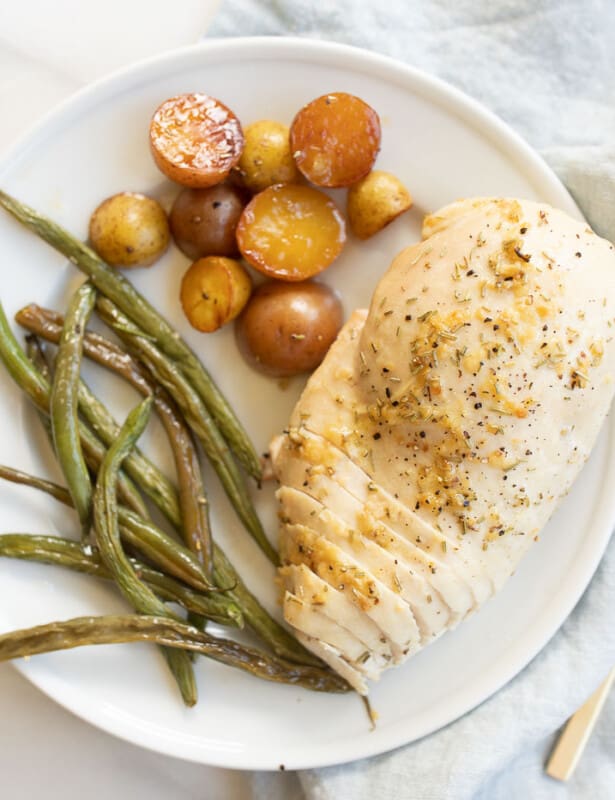 White plate with a marble counter in the background, filled with baked rosemary chicken, green beans and baby potatoes. #rosemarychicken #lemonrosemarychicken #bakedchickenandveggies
