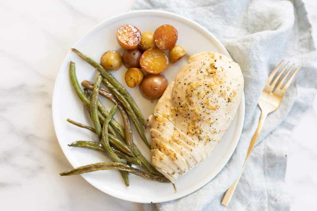 White plate with a marble counter in the background, filled with baked rosemary chicken, green beans and baby potatoes. #rosemarychicken #lemonrosemarychicken #bakedchickenandveggies