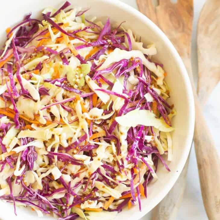 White salad bowl filled with colorful cabbage salad and wooden serving spoons. #cabbagesalad