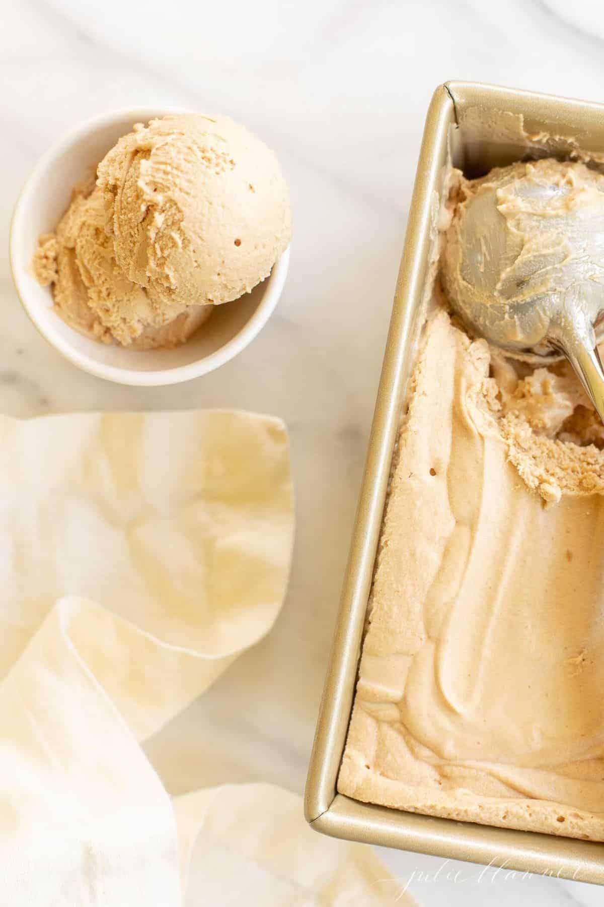Gold pan filled with ice cream, scoop of ice cream in a bowl to the side. #cookiebuttericecream #speculoosicecream