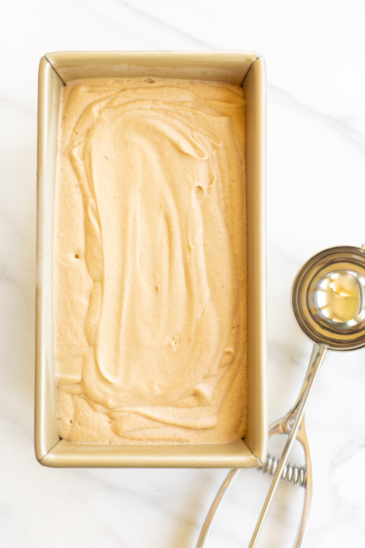 A gold loaf pan full of homemade no churn cookie butter ice cream.
