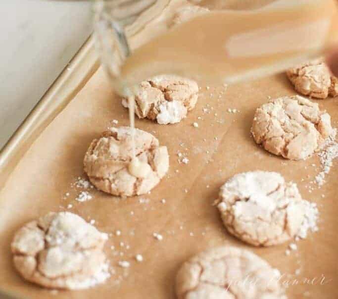 A glass jar pouring apple glaze onto cookies on a gold baking sheet. #appleglaze #appleciderglaze