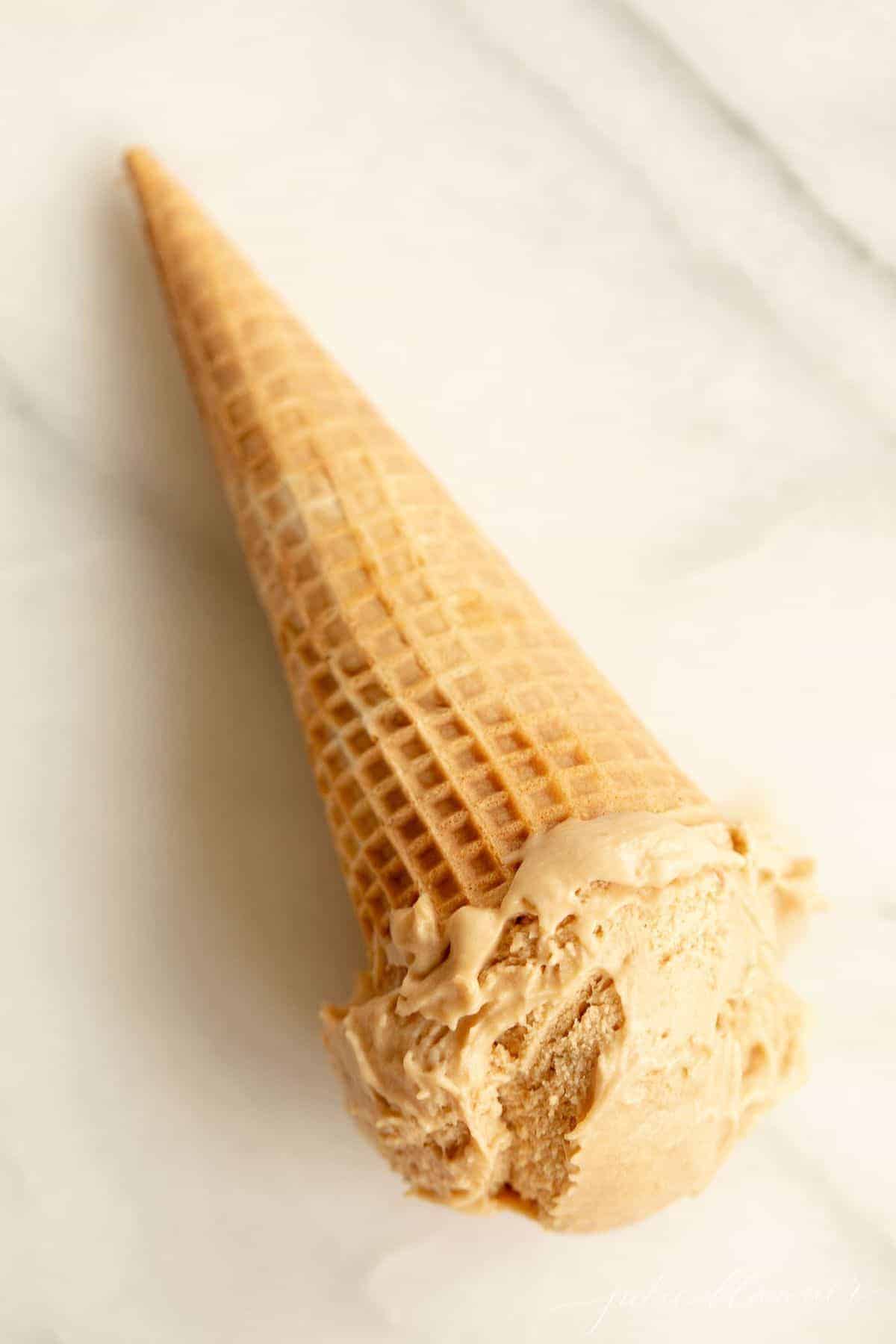A waffle ice cream cone on a marble surface, filled with homemade speculoos ice cream. #cookiebuttericecream
