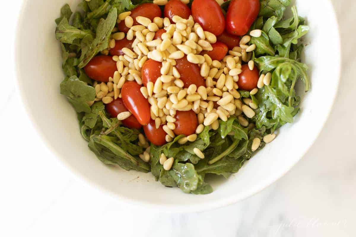 White salad bowl filled with arugula, pine nuts and grape tomatoes.