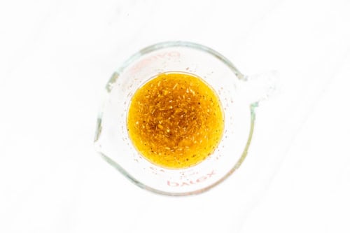 Top view of a glass beaker containing an amber-colored liquid, set against a white background with Italian vegetables.