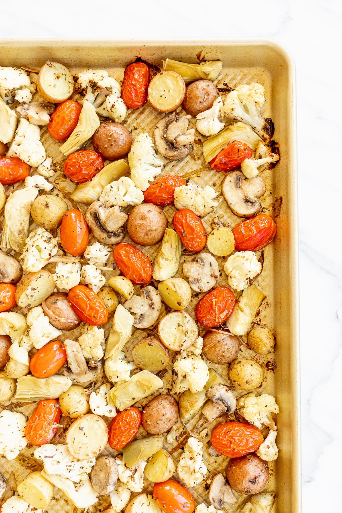 Roasted Italian vegetables and sausages on a baking sheet, including cauliflower, tomatoes, mushrooms, and artichokes.