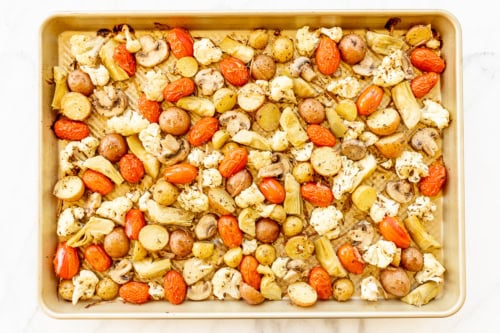 A baking sheet with Italian roasted vegetables including potatoes, cauliflower, mushrooms, and cherry tomatoes, seasoned and spread out evenly.