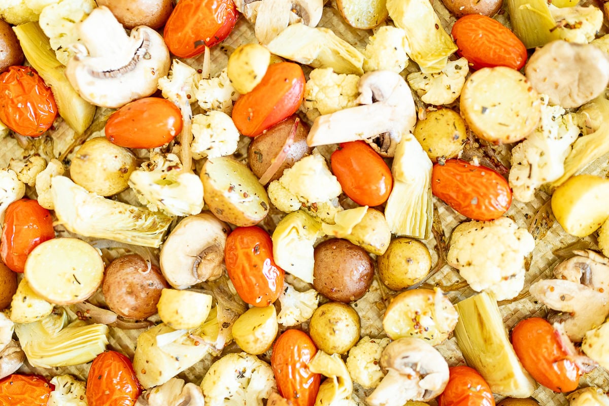 Close-up of Italian roasted vegetables including mushrooms, cherry tomatoes, cauliflower, and potatoes seasoned with herbs.