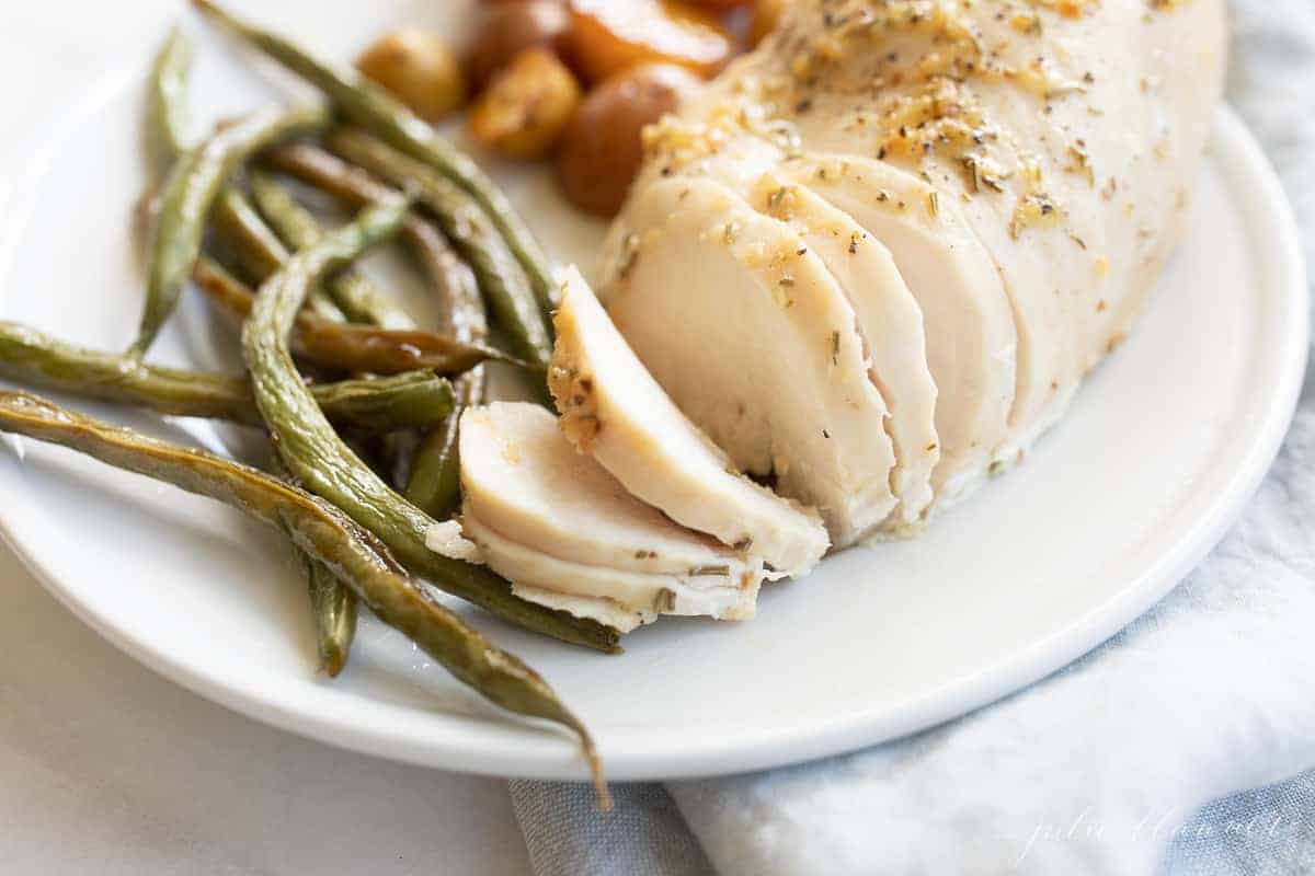 White plate close-up, filled with baked rosemary chicken, green beans and baby potatoes. #rosemarychicken #lemonrosemarychicken #bakedchickenandveggies