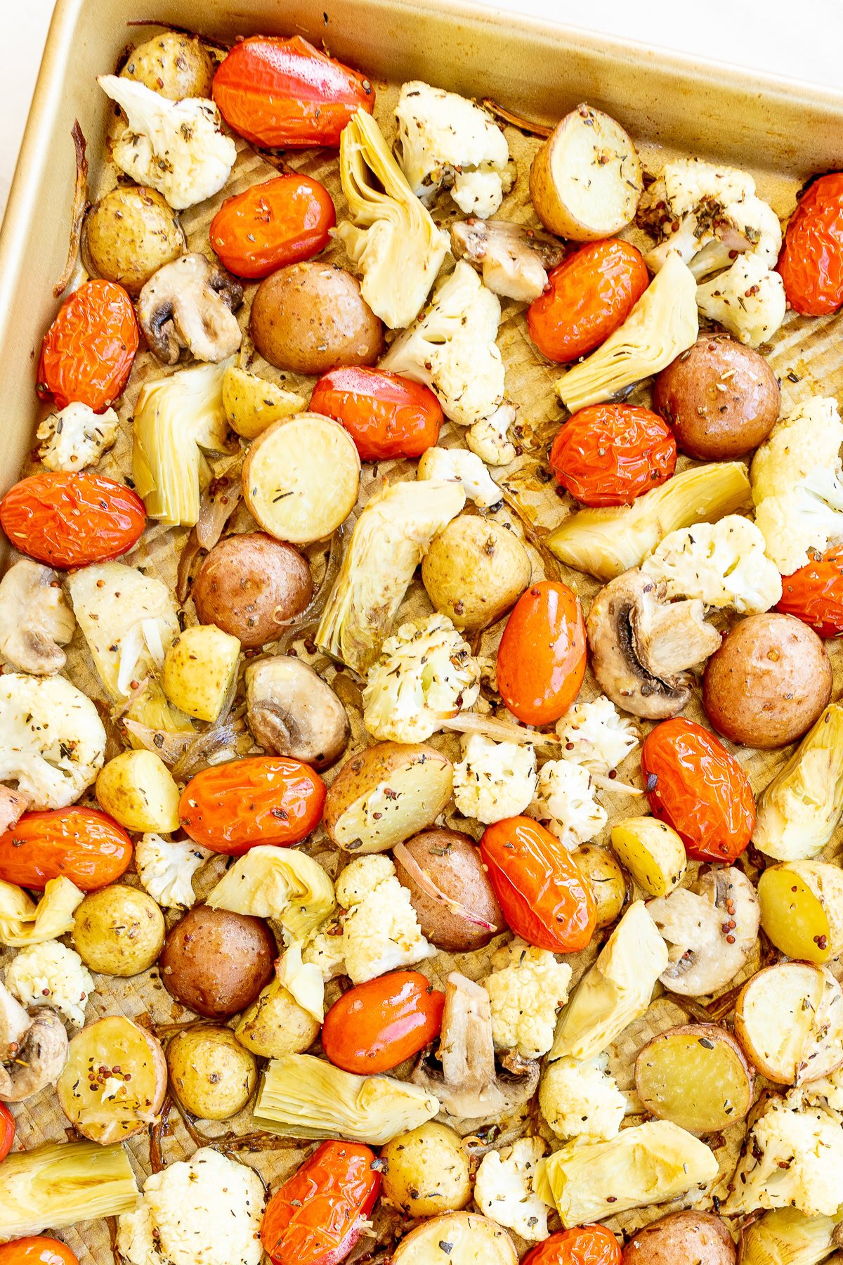 Roasted Italian vegetables and sausages on a baking sheet, including cauliflower, tomatoes, mushrooms, and artichokes.