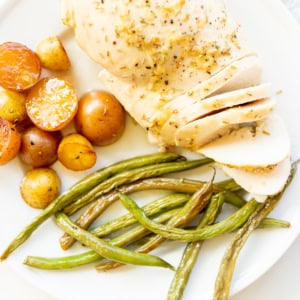 A plate with sliced rosemary chicken breast, green beans and baby potatoes.