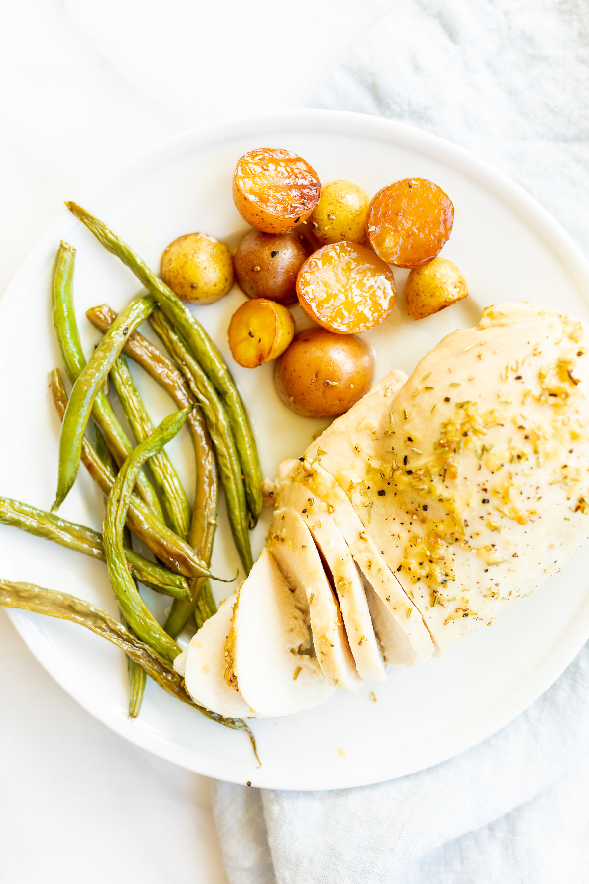 A plate with sliced rosemary chicken breast, green beans and baby potatoes.