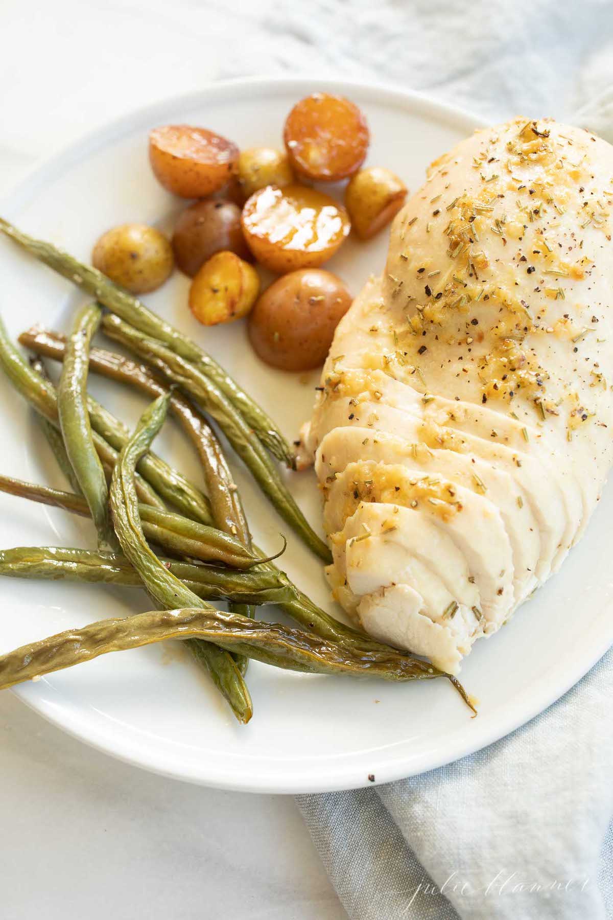 A white plate with rosemary chicken, potatoes and green beans.