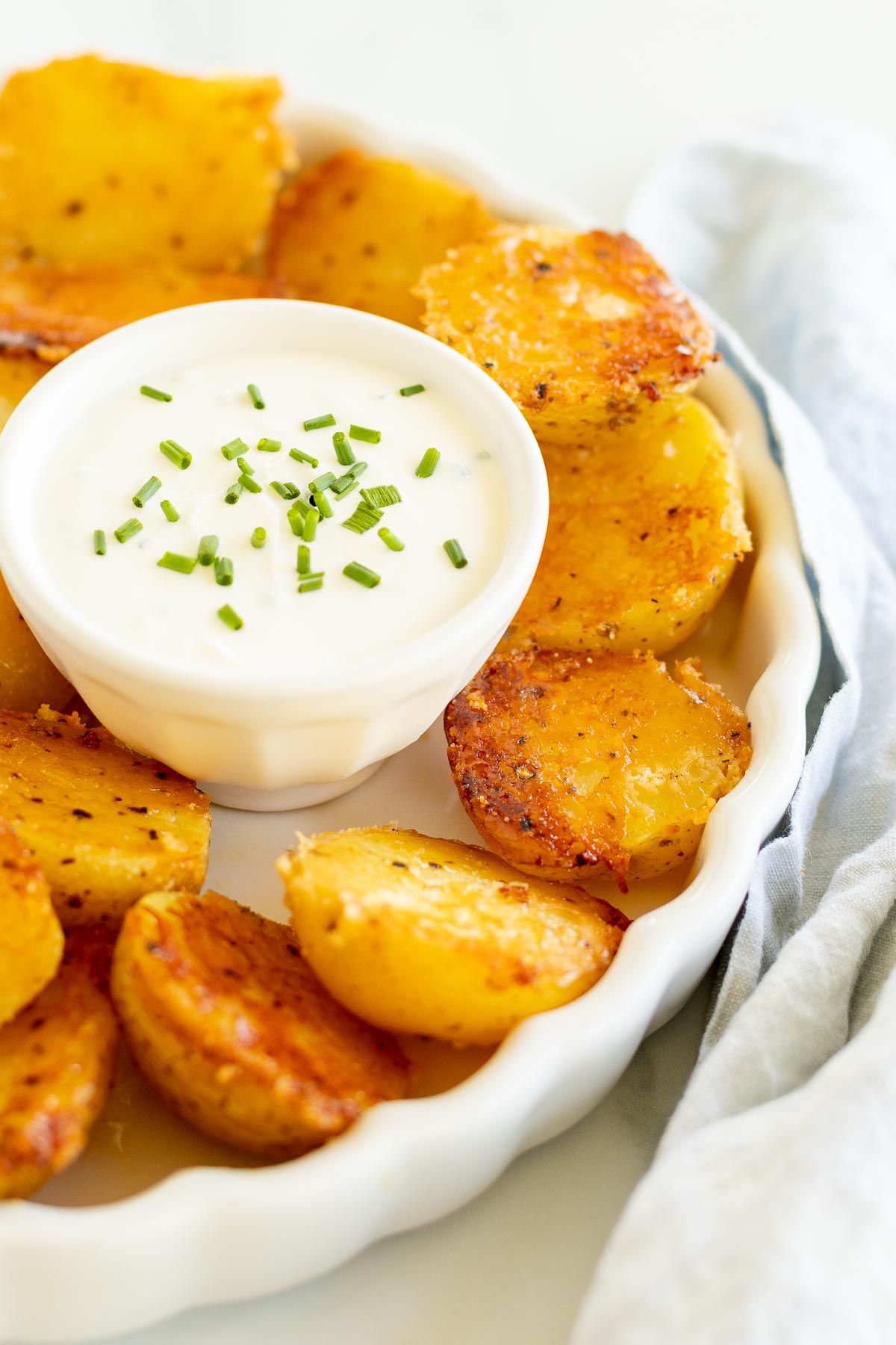 Sour cream dip in a small white bowl, surrounded by parmesan potatoes