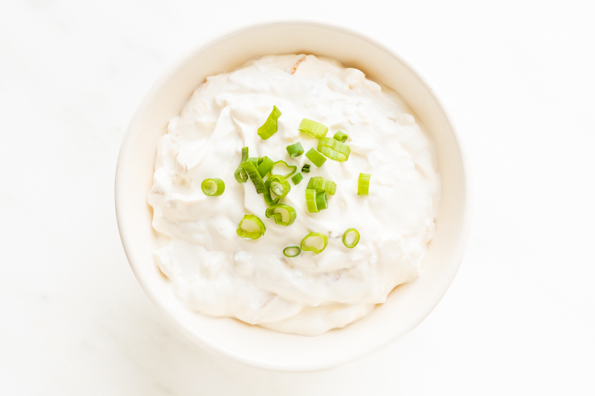 A white bowl full of sour cream dip, topped with chopped green onions.