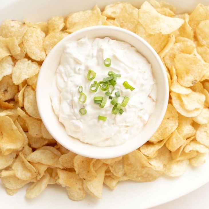 A white oval platter with a bowl of sour cream dip in the center of potato chips.