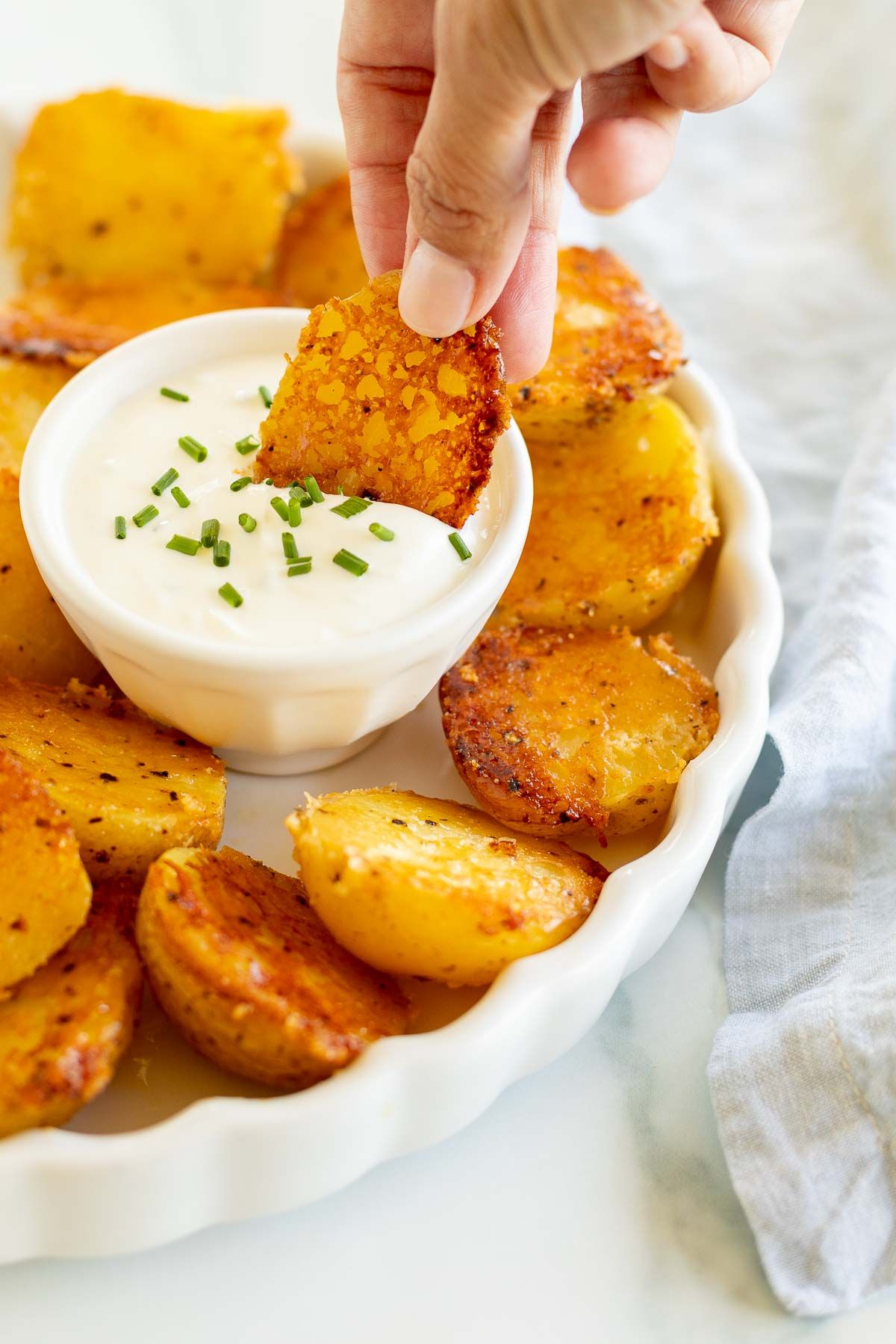 A crispy potato dipping into a bowl of sour cream dip.