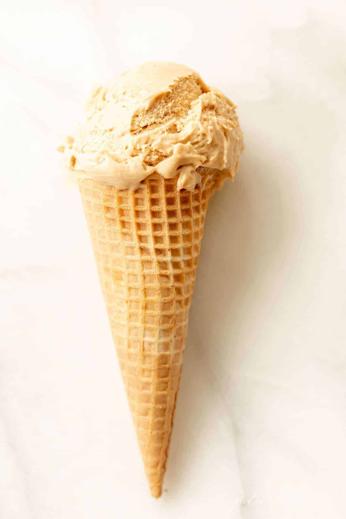 A waffle ice cream cone on a marble surface, filled with homemade speculoos ice cream. #cookiebuttericecream