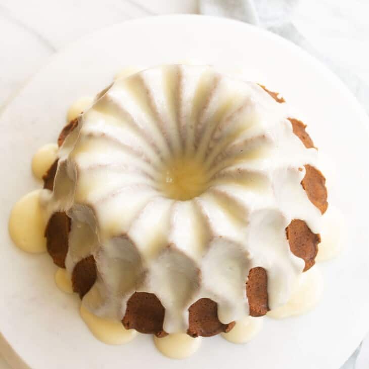 a bundt cake on a marble platter, covered in white glaze.
