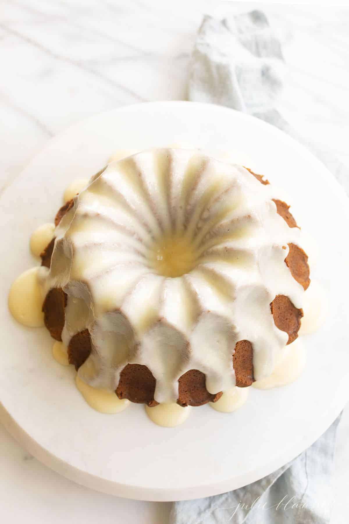 a bundt cake on a marble platter, covered in white glaze.
