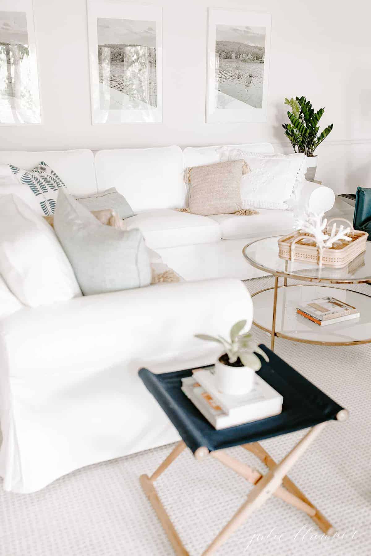 Living room scene with a white sectional, large photos on the wall and a wooden side table featuring a houseplant. #zzplant #zzplantcare